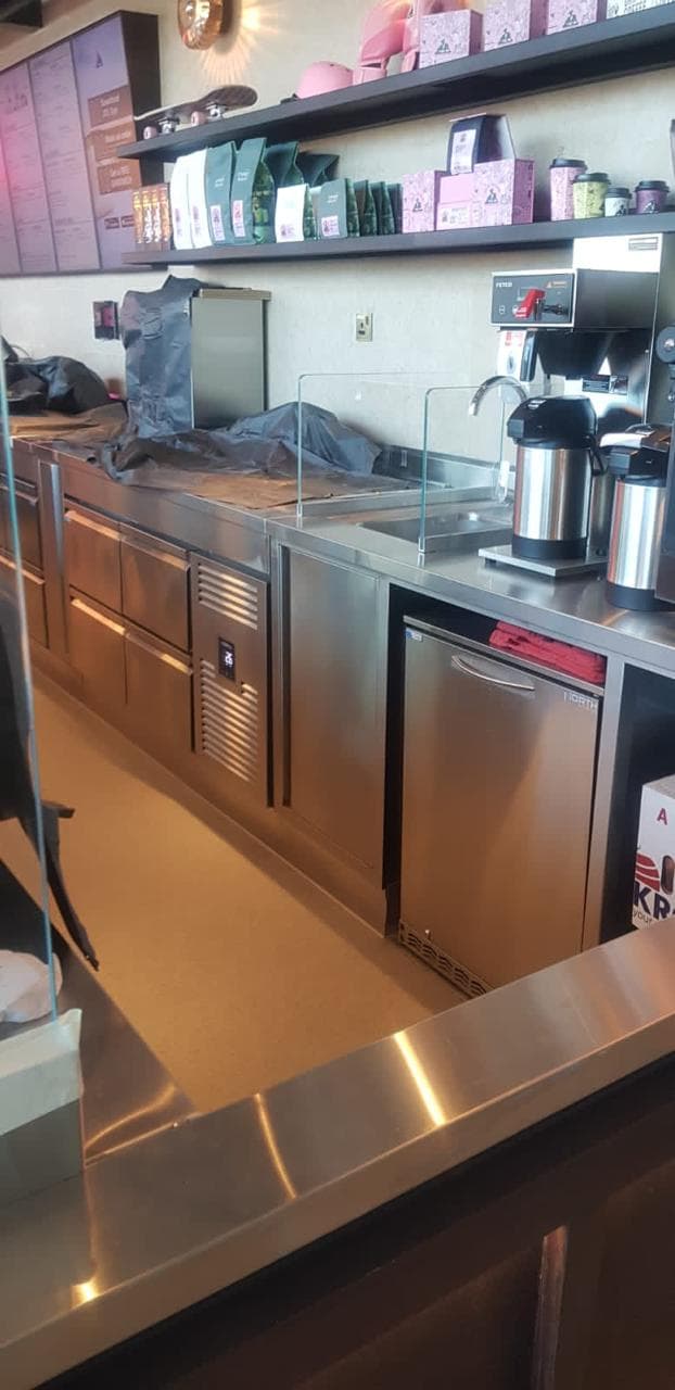 Completed cafe service counter with stainless worktops, refrigerated bases, coffee brewers and stocked retail shelving, supplied and installed by FMR Technical Services, Dubai